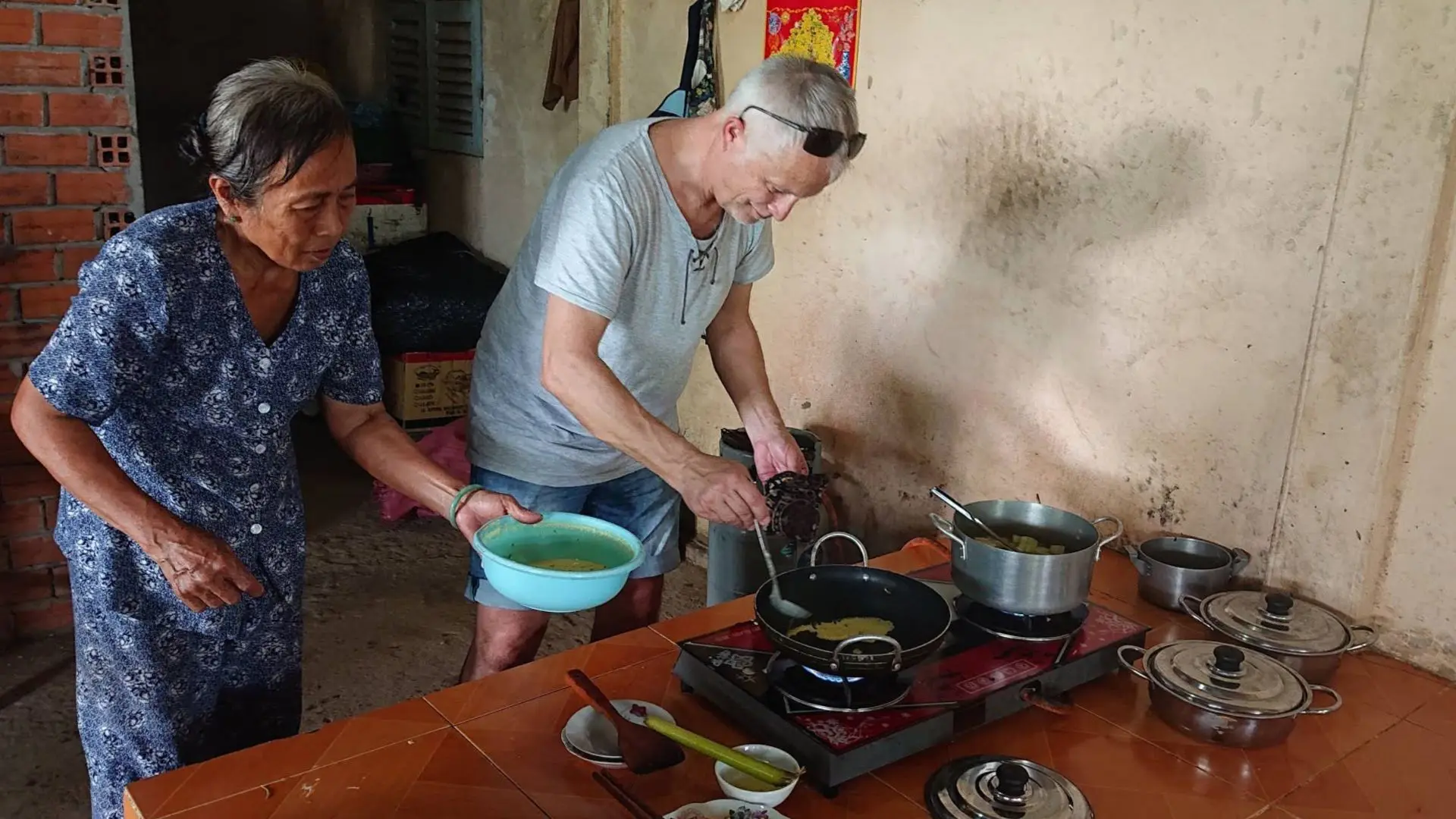 An elderly local woman teaching a tourist how to cook traditional Mekong dishes over a stove on Tan Phong Islet