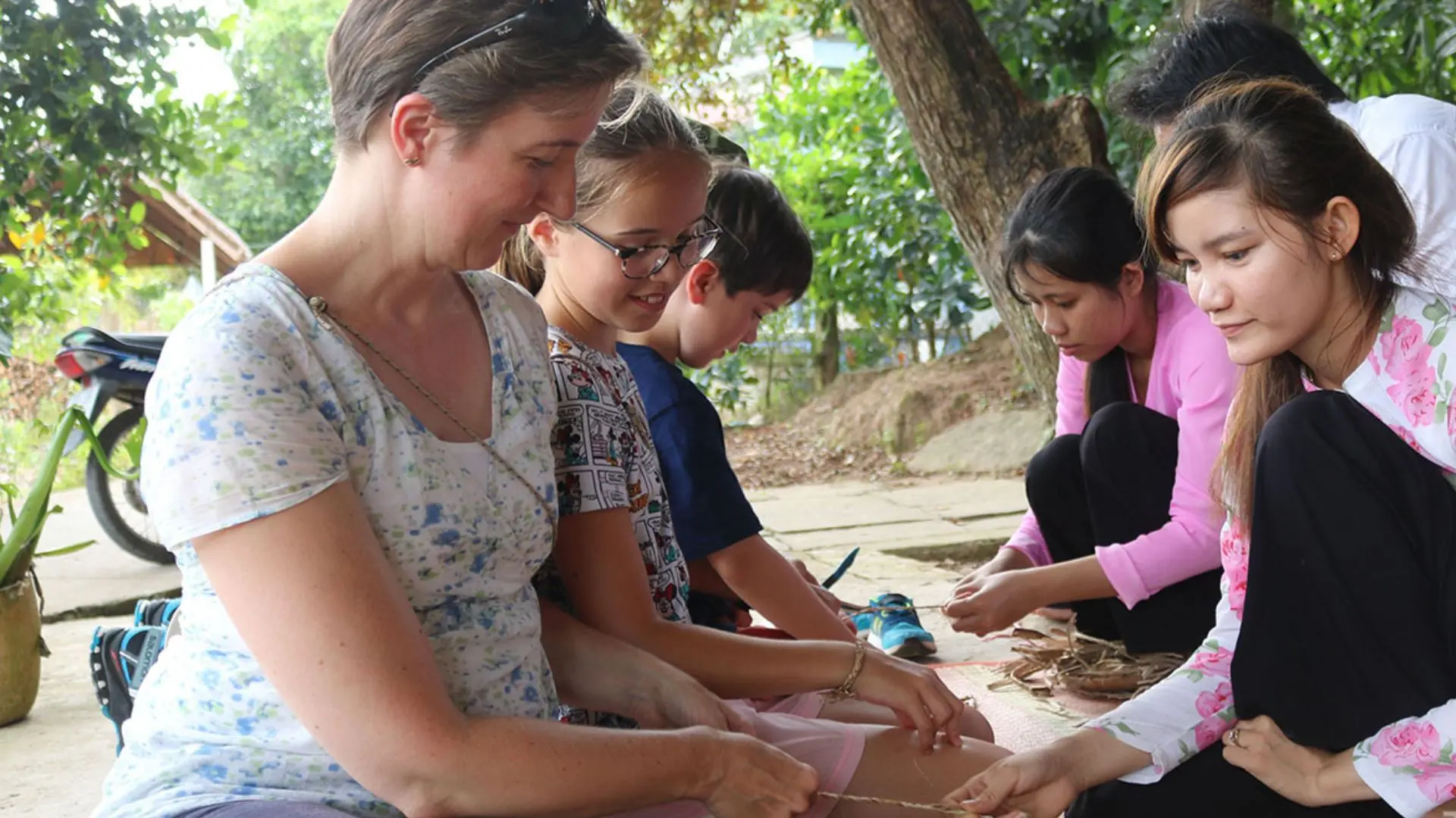 International visitors sitting with local Vietnamese women learning to weave traditional handicrafts on Tan Phong Islet