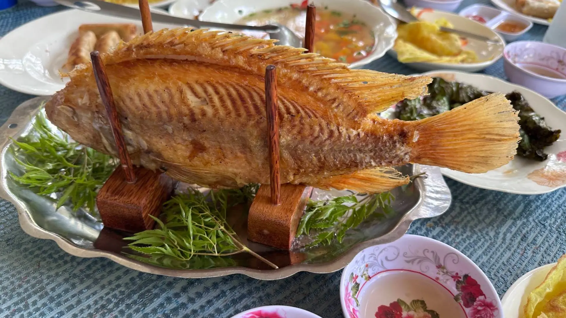 A platter featuring a crispy deep-fried elephant ear fish served with fresh herbs and dipping sauce on Tan Phong Islet