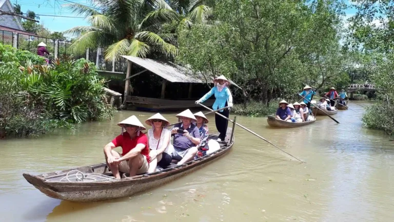 A group of tourists wearing conical hats on a sampan boat being rowed through a narrow canal on Tan Phong Islet