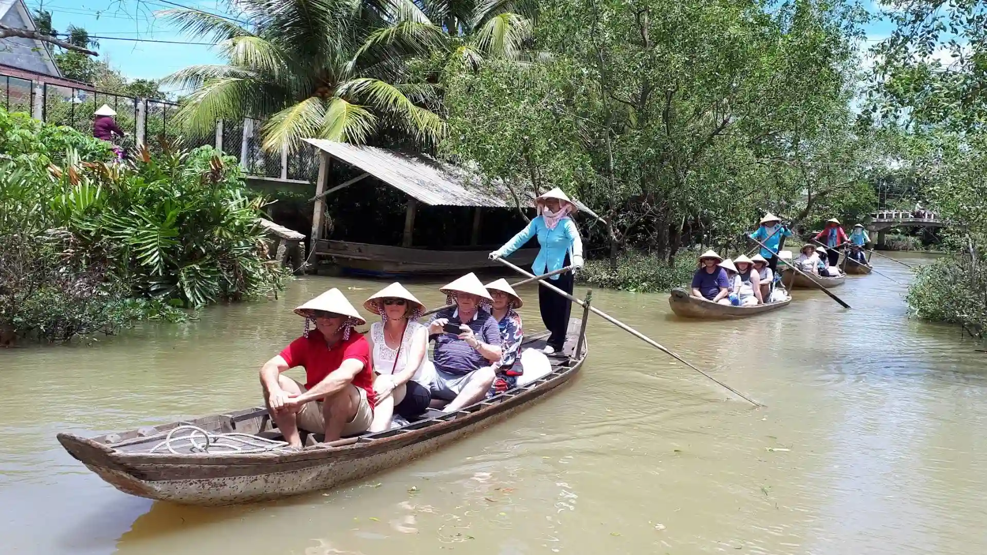 Tan Phong Islet: Cai Be’s Rambutan Kingdom & Eco-Paradise 163 A group of tourists wearing conical hats on a sampan boat being rowed through a narrow canal on Tan Phong Islet
