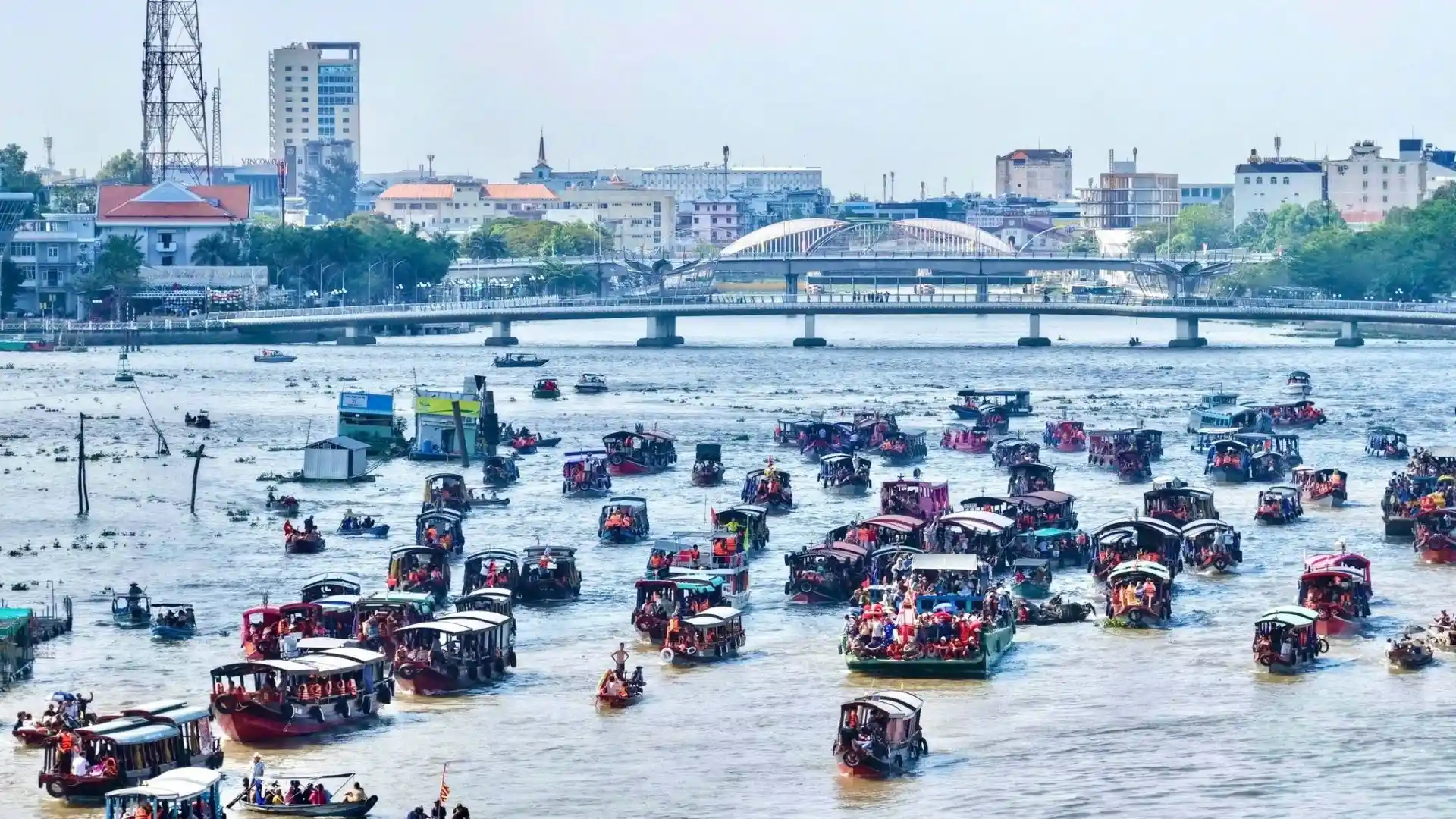 Floating boats participating in Tong Phong Festival parade on Can Tho river with cityscape in background