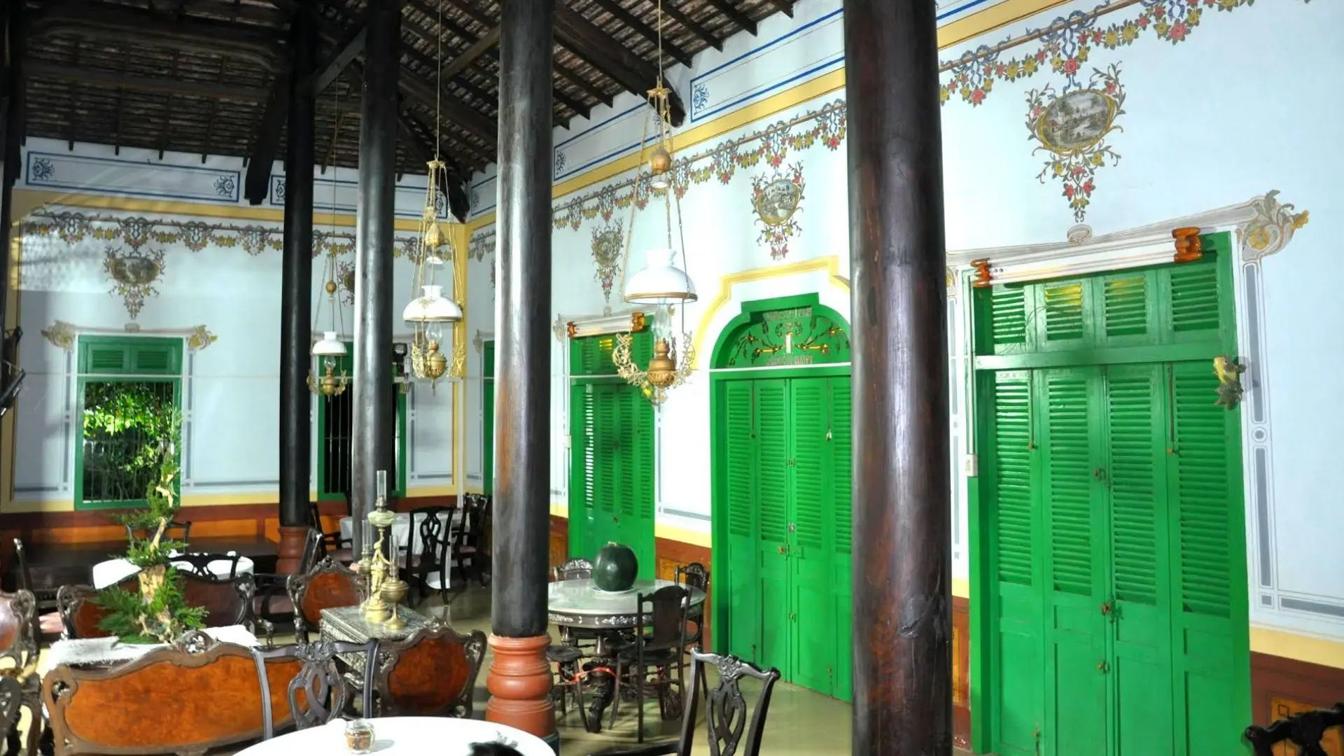 Wide view of the interior hall of Ba Duc Ancient House with dark wooden pillars and vintage green doors