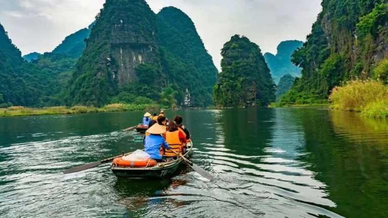 Visitors traveling by boat along a river surrounded by limestone mountains in Ninh Binh