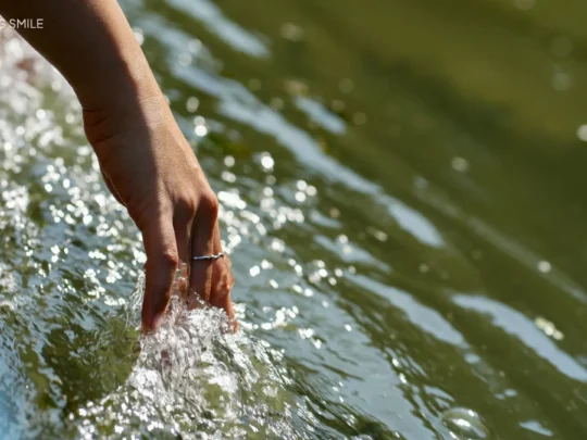 A tourist's hand reaching into the clear water, touching a layer of bright green duckweed